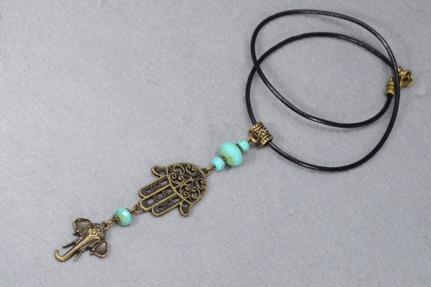 Boho chic leather cord with intricate bronze pendant & sea green Czech glass, perfect for adding flair to any outfit. Estibela design.