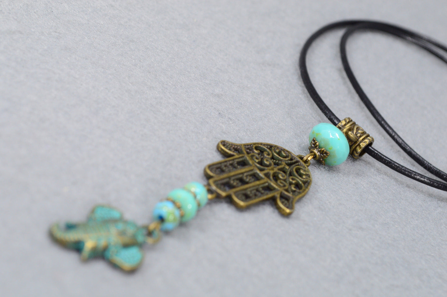 Boho chic leather cord with intricate bronze pendant & sea green Czech glass, perfect for adding flair to any outfit. Estibela design.